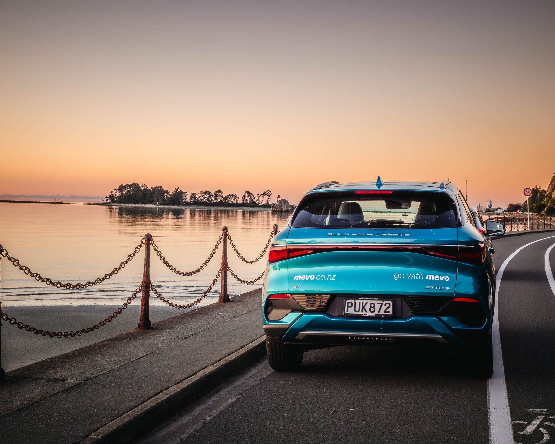 Blue car on a road by a waterfront at sunset